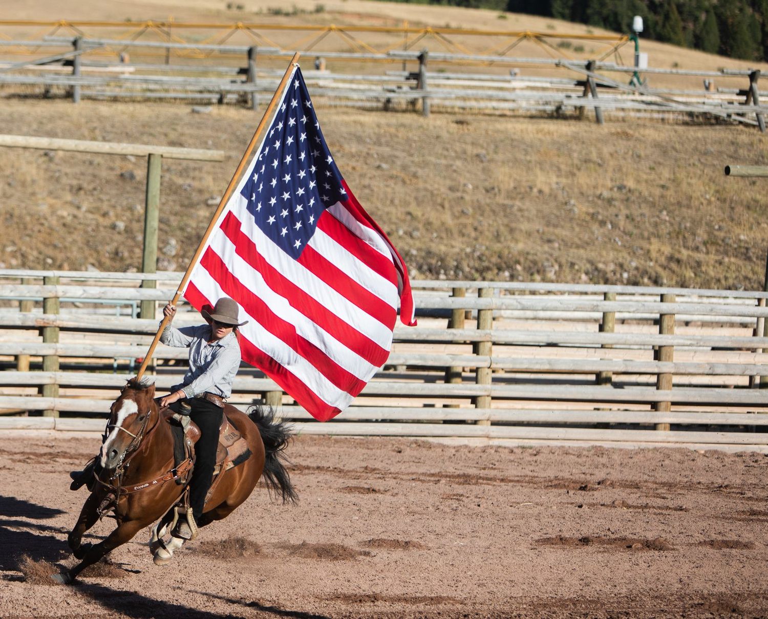 A rider carrying the American flag at a gallop across a rodeo arena