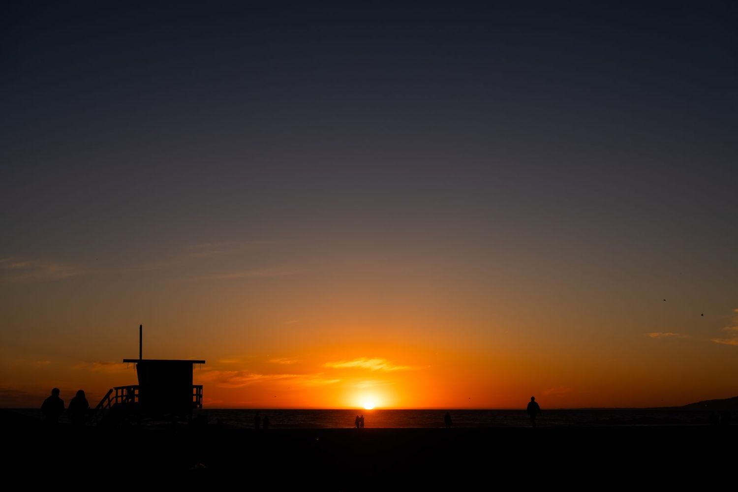 A lifeguard tower silhouetted against the setting sun over the Pacific